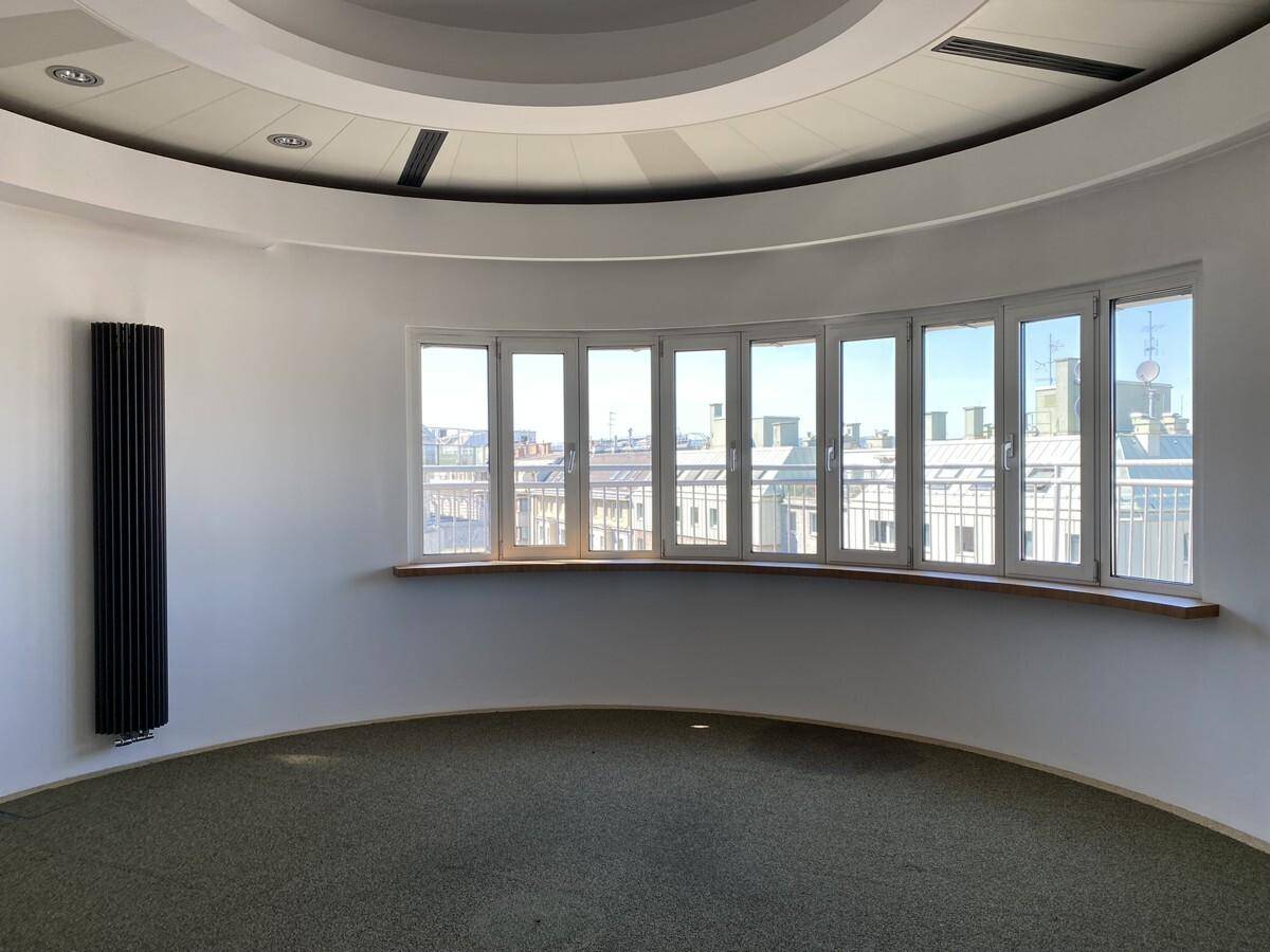 Heller, runder Büroraum mit großen Fenstern, die einen weiten Blick über die Stadt bieten, und einem modernen Heizkörper.