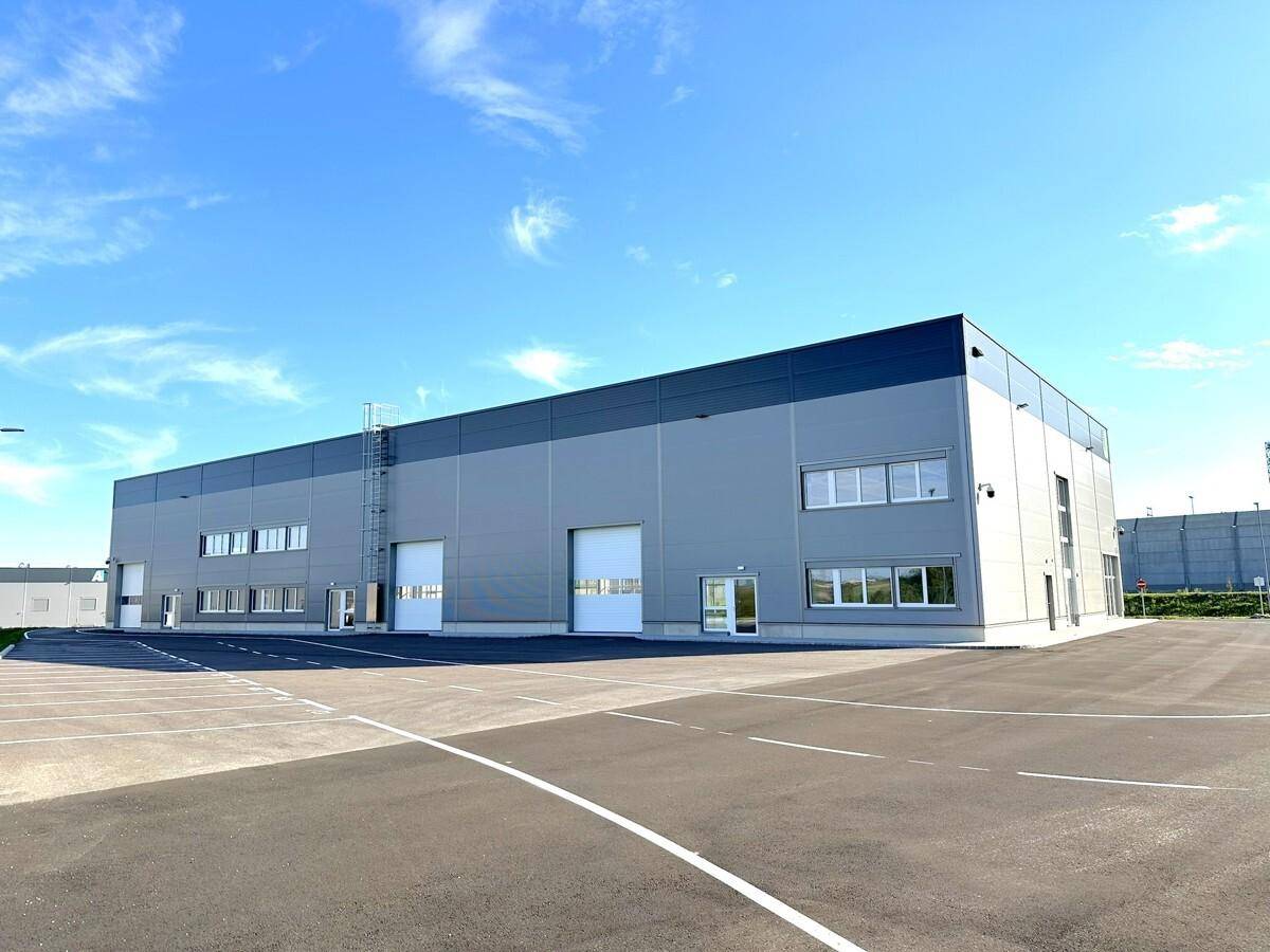 Weitläufiges modernes Geschäftsgebäude mit mehreren Rolltoren und großem Parkplatz unter blauem Himmel.