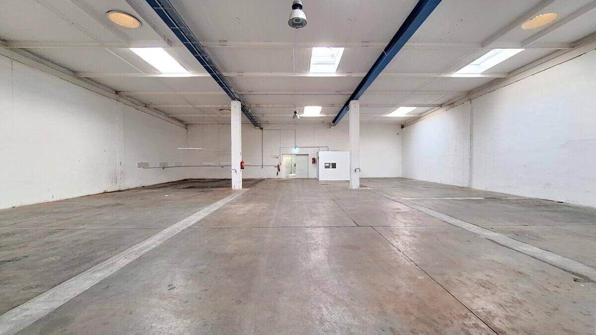 Weitläufige, leere Lagerhalle mit Betonboden, hohen Decken und mehreren Oberlichtern.