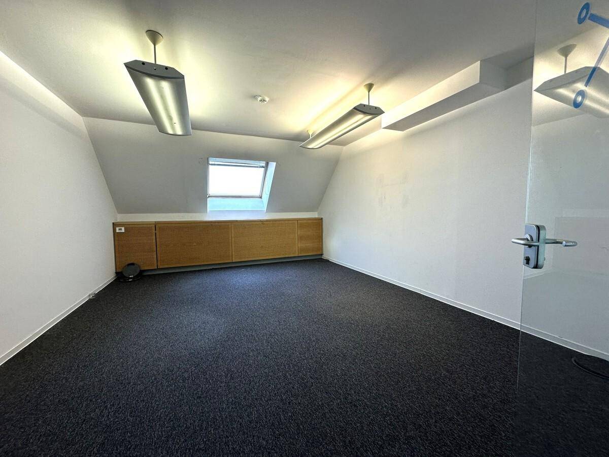 Heller Büroraum im Dachgeschoss mit Teppichboden, Dachfenster und Einbauschränken.