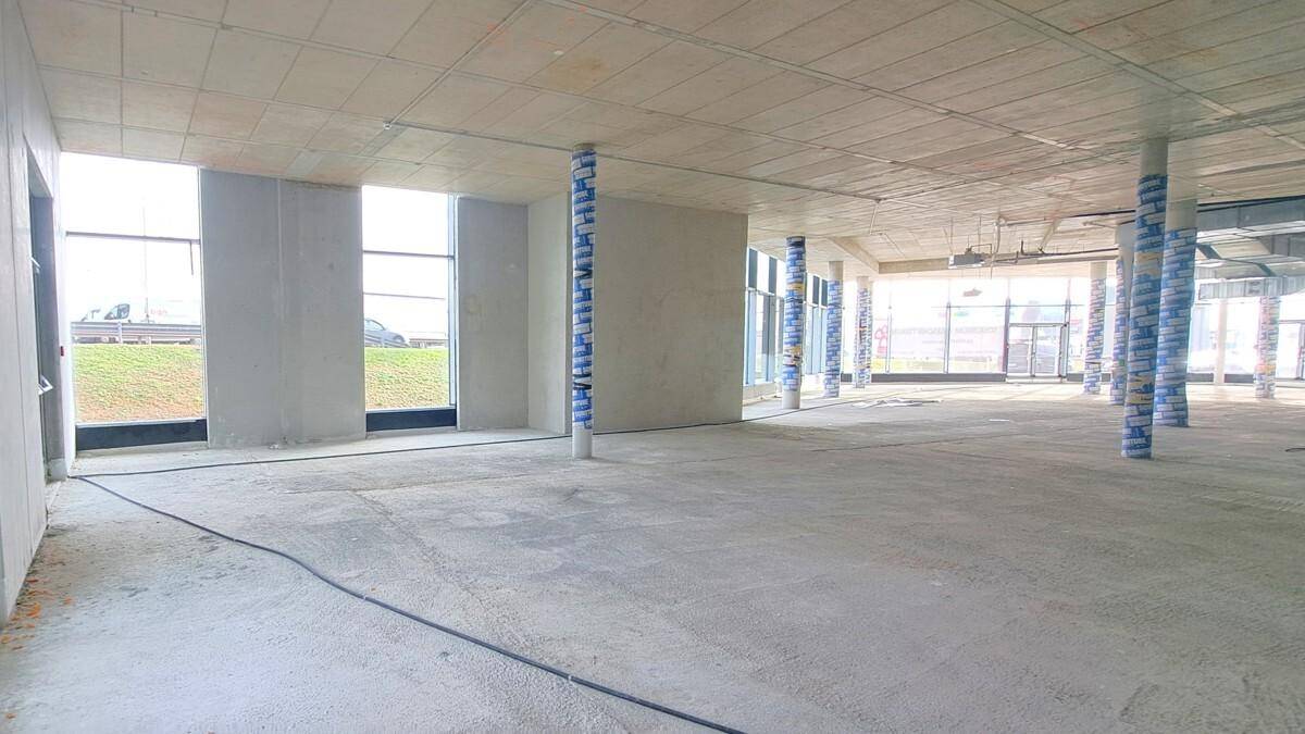 Unfertiger Gewerberaum mit Betonwänden, großen Fenstern und einem weiten Blick nach draußen, ideal für individuelle Gestaltung.