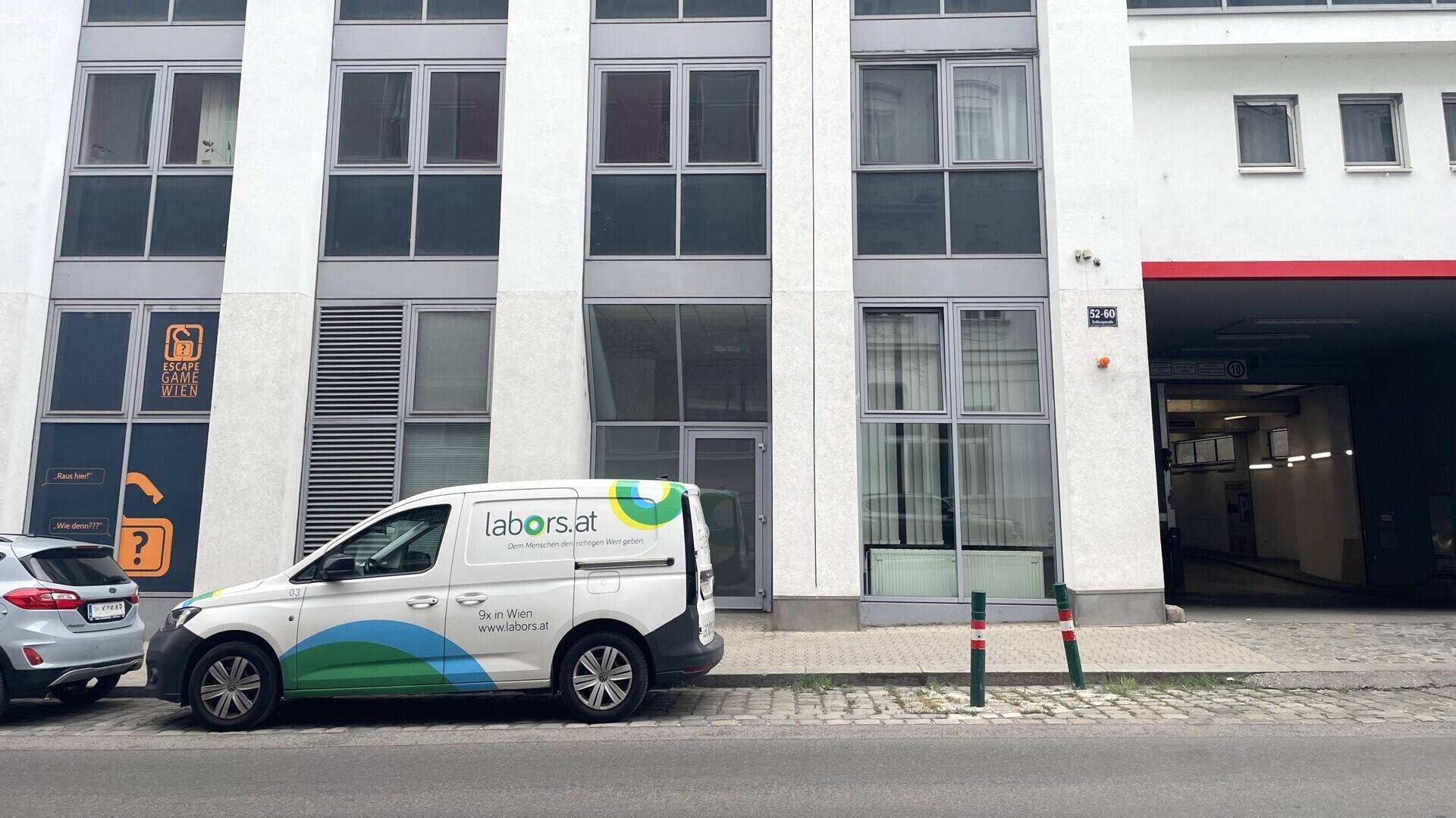 Nahaufnahme der modernen Gebäudefassade mit großen Fenstern und dem Eingang zur Tiefgarage auf Straßenniveau.