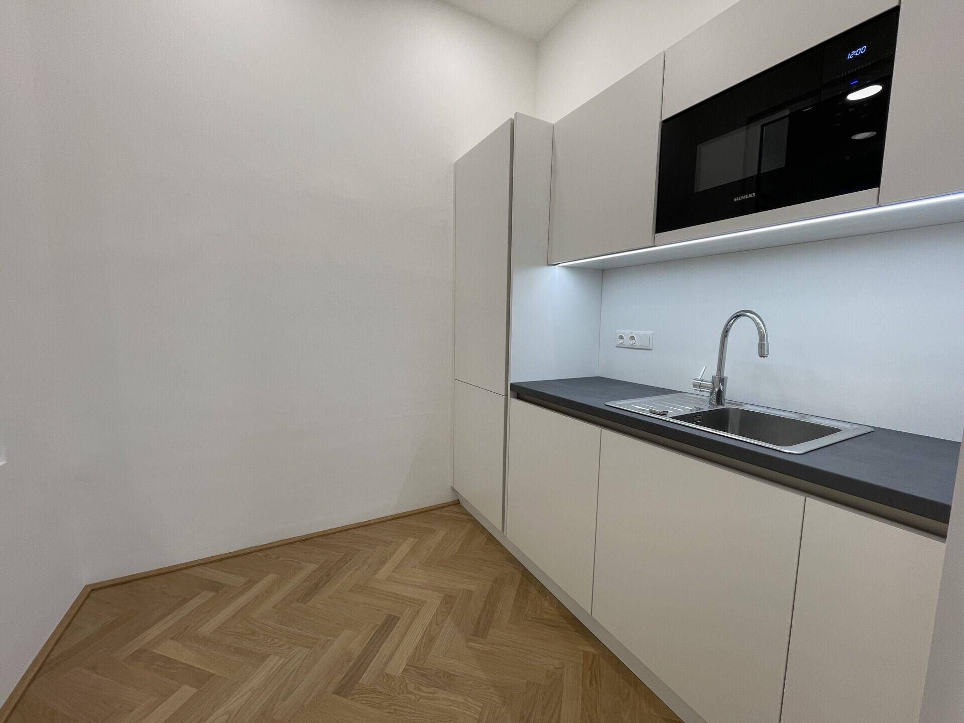 Moderne Küchenzeile mit weißen Schränken, dunkler Arbeitsplatte und integrierter Mikrowelle, sehr funktional.