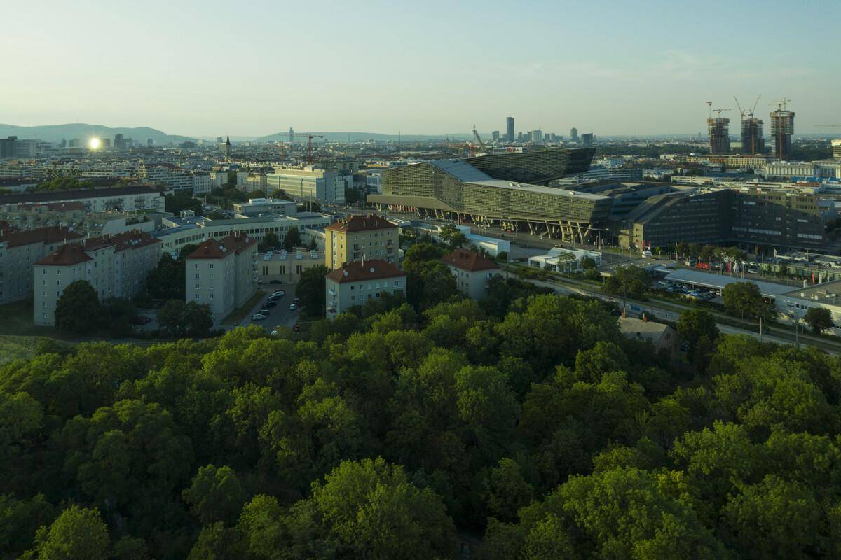 Luftaufnahme einer Stadtlandschaft mit modernen Gebäuden, viel Grün und einem weiten Blick auf die Skyline.