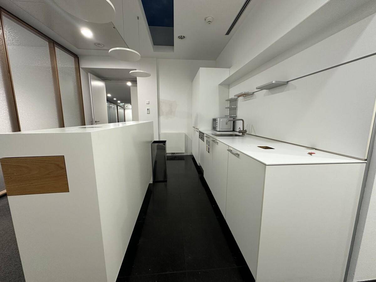 Moderne Teeküche mit weißen Schränken, schwarzem Boden und integrierten Geräten, ideal für Mitarbeiterpausen.