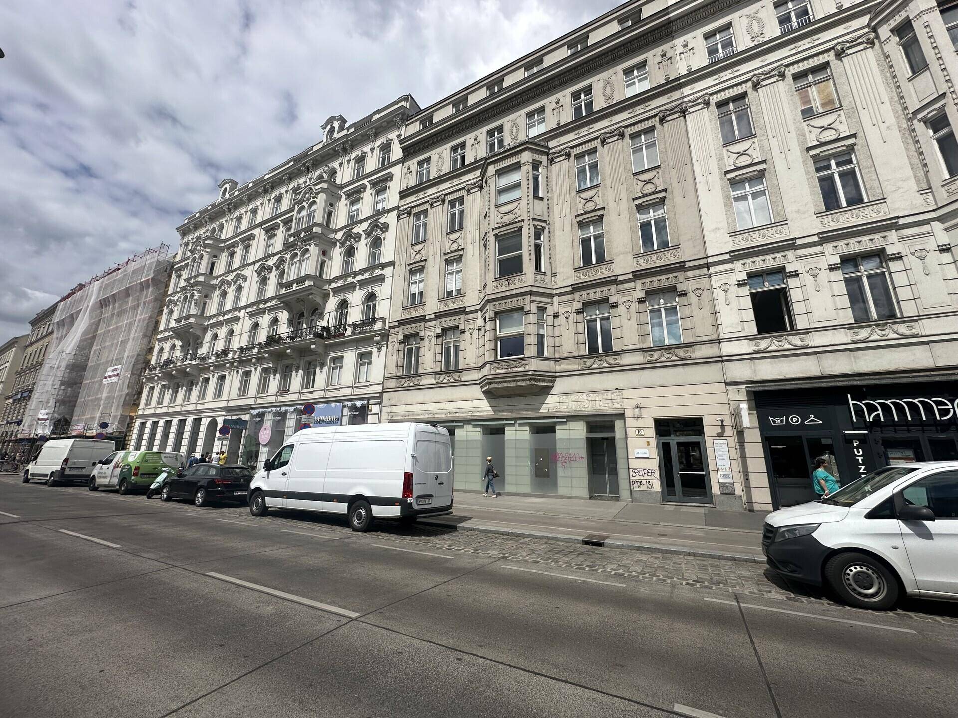 Weitwinkelaufnahme der historischen Gebäudefassade entlang der Straße mit parkenden Fahrzeugen.