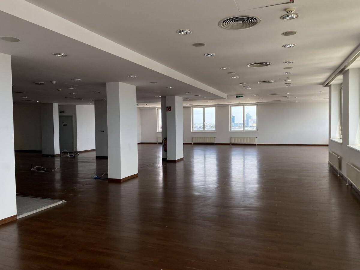 Geräumiger Bürobereich mit dunklem Holzfußboden, Säulen und vielen Fenstern.