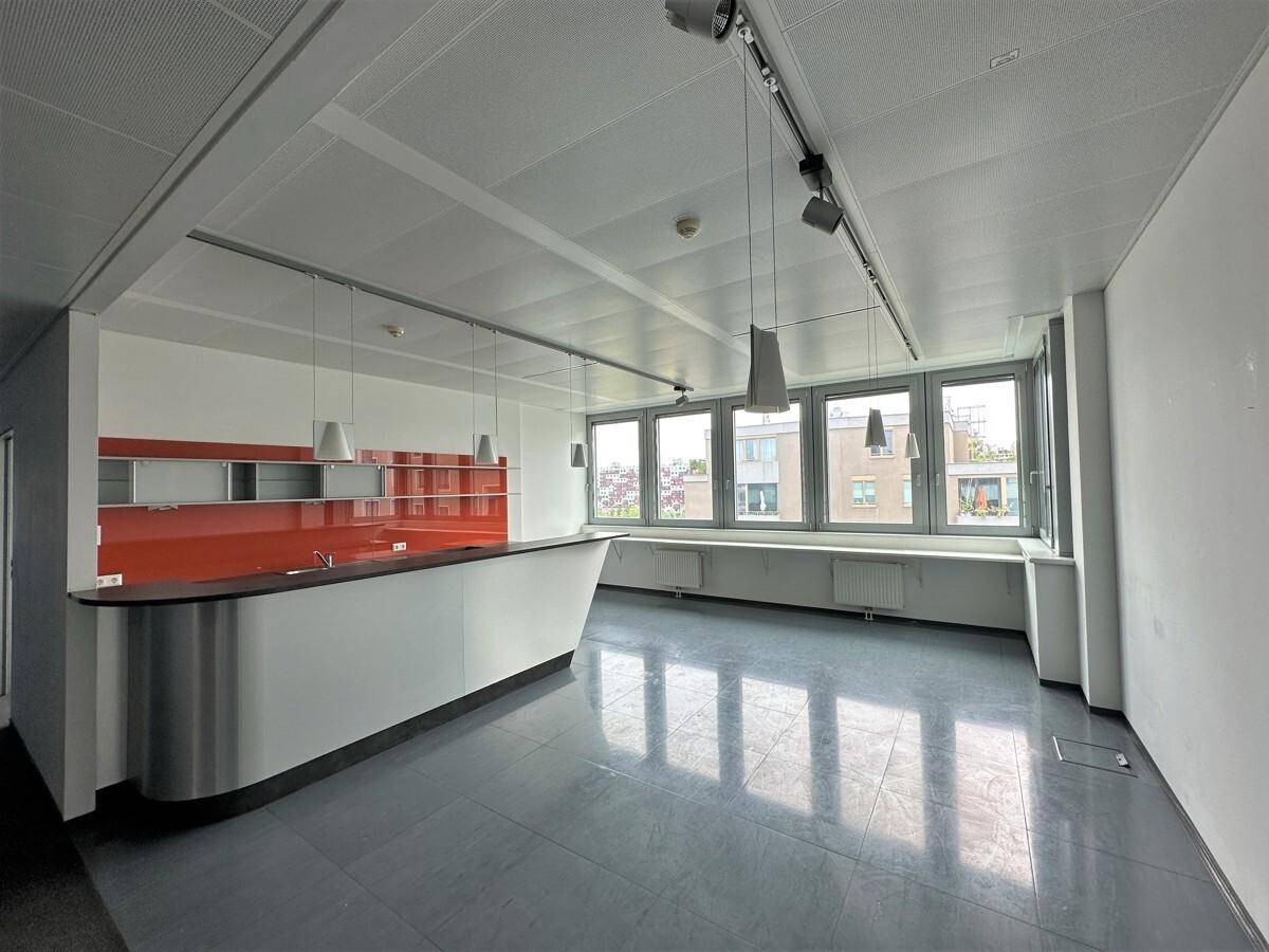 Helle Teeküche mit moderner Theke, orangefarbener Rückwand und großen Fenstern mit Stadtblick.
