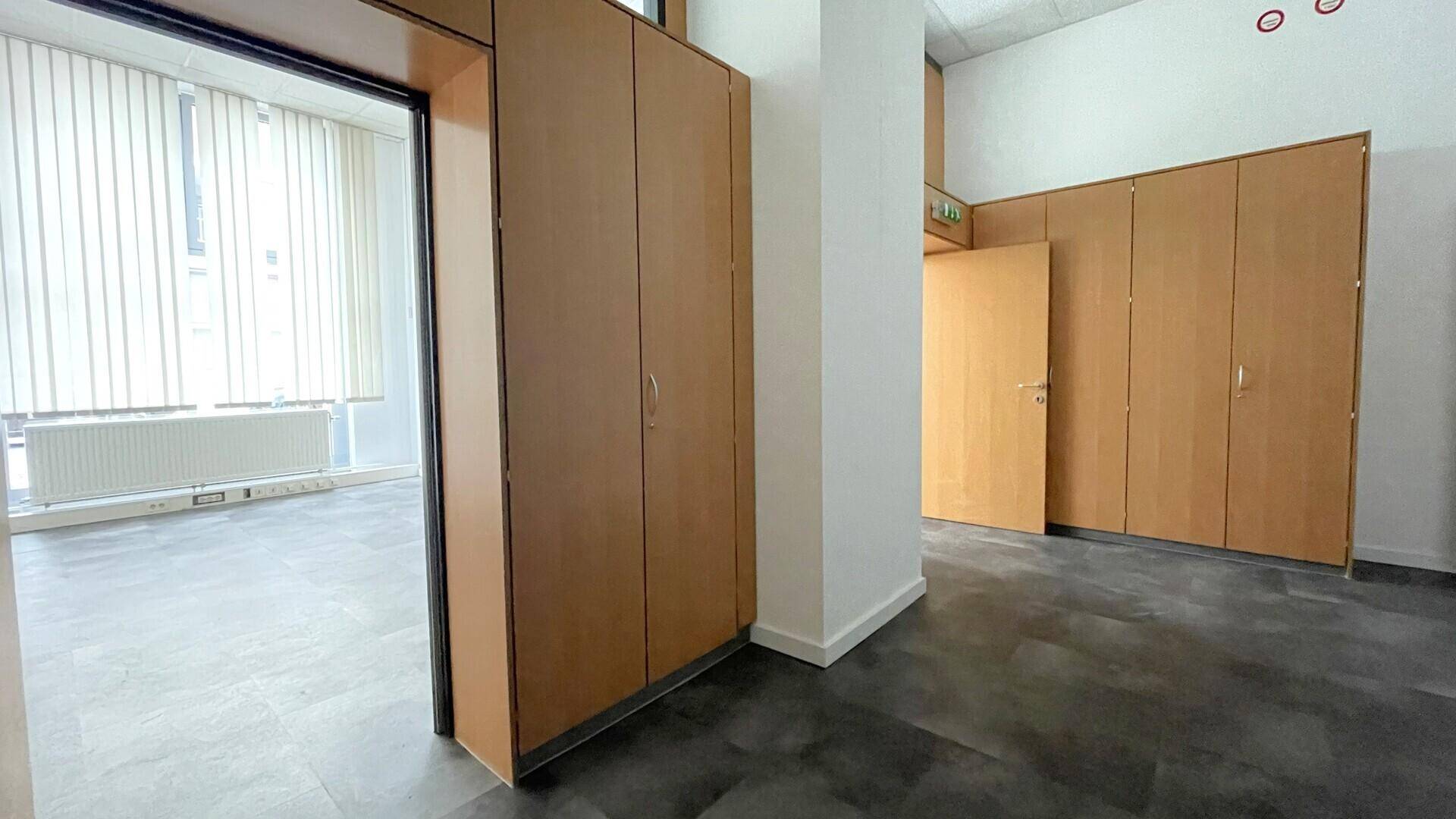 Büroraum mit integrierten Holzschränken, dunklem Boden und Blick auf die Fenster mit Jalousien.