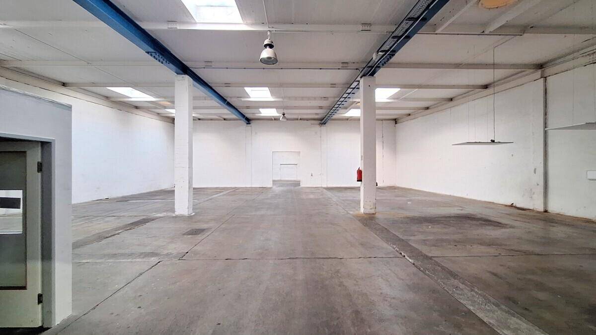 Große, leere Lagerhalle mit hohen Decken, Betonboden und Oberlichtern für natürliches Licht.