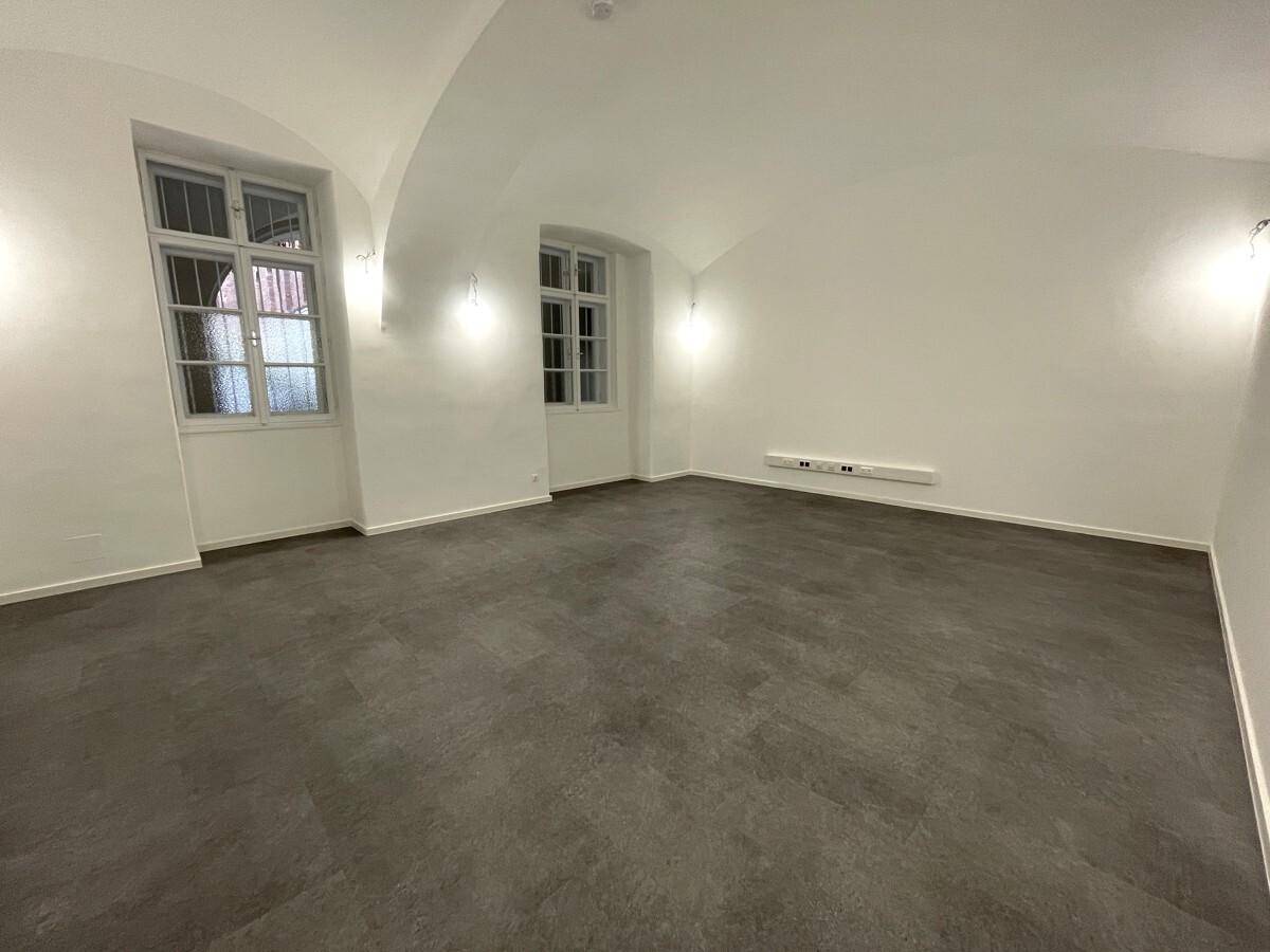 Langer, schmaler Raum mit einer eleganten Gewölbedecke, einem Fenster und neuem, pflegeleichtem dunklem Bodenbelag.