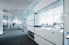 Heller, moderner Bürobereich mit Glaswänden, weißen Schränken und Teppichboden.