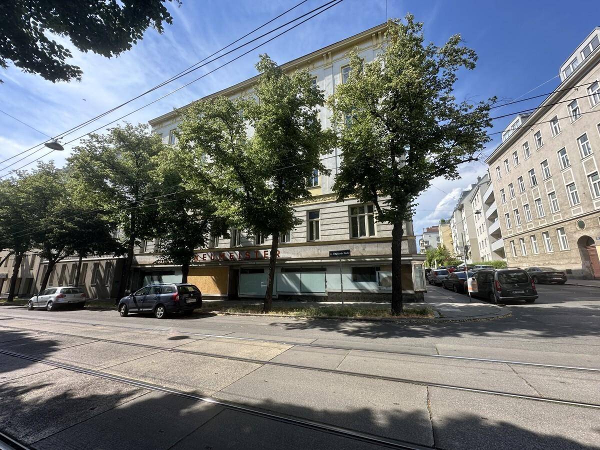 Eine weitere Perspektive des Gebäudes an der Straßenecke, mit Bäumen und parkenden Fahrzeugen im Vordergrund.
