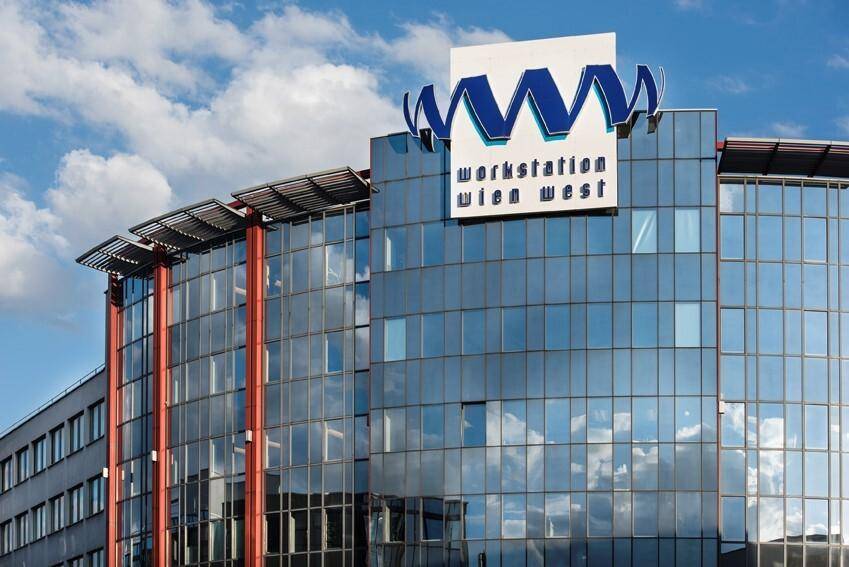 Nahaufnahme der modernen Glasfassade eines Bürogebäudes mit dem Firmenlogo unter bewölktem Himmel.