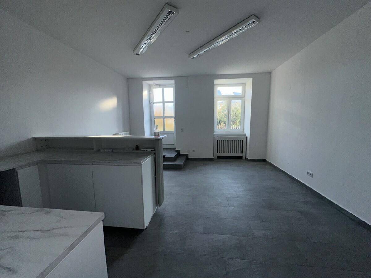 Geräumiger Bürobereich mit grauen Fliesen, einer Theke und großen Fenstern, die viel Tageslicht hereinlassen.