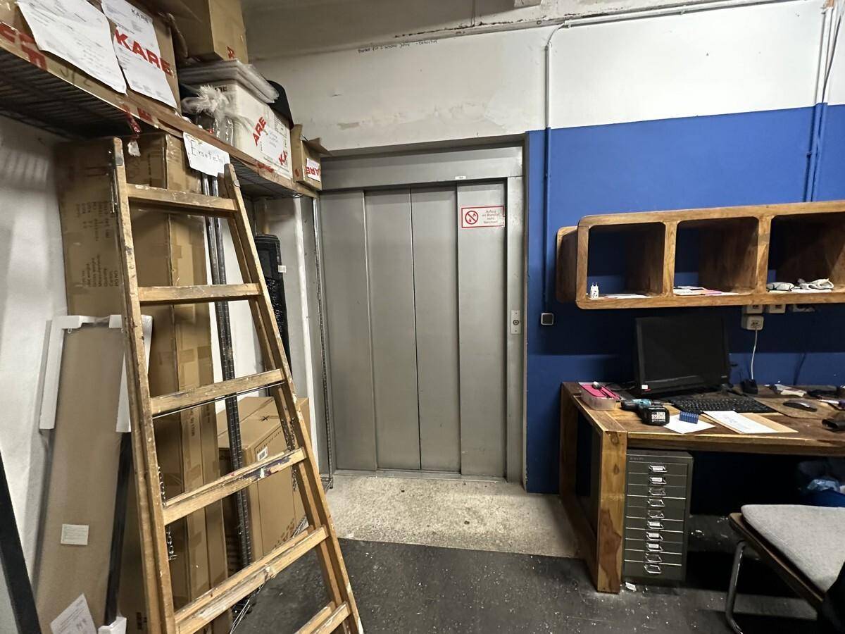 Kleiner Bürobereich neben einem Lastenaufzug in einem Lagerraum mit blauer Wand.