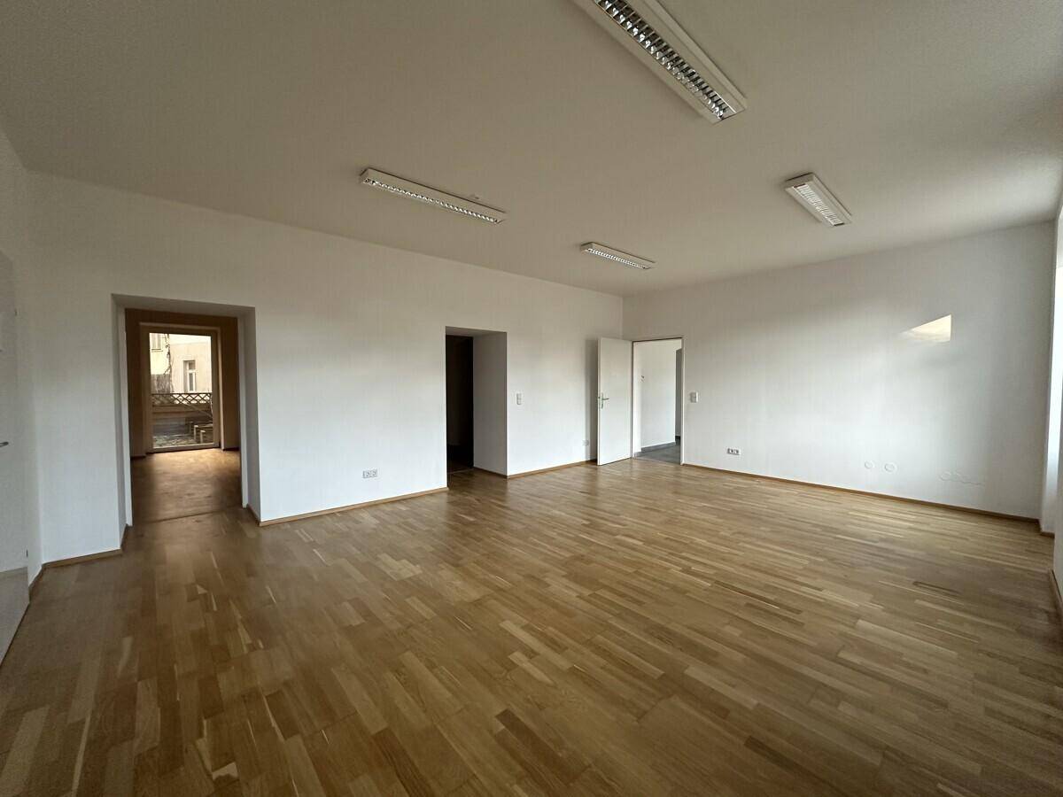 Großer, heller Büroraum mit Parkettboden und mehreren Türen, die zu anderen Räumen führen.