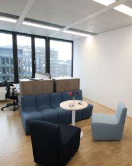 Gemütlicher Loungebereich mit blauen Sofas, kleinem Tisch und großen Fenstern mit Stadtblick.