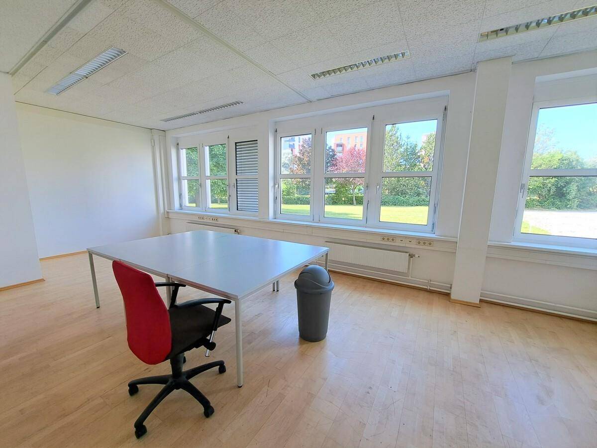 Modernes Büro mit Laminatboden, großem Schreibtisch und Bürostuhl, hell durch große Fenster.