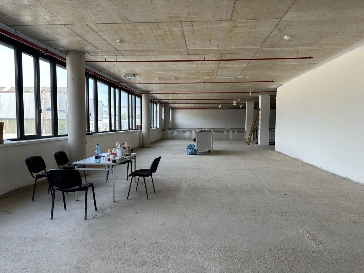 Heller, unfertiger Gewerberaum mit großen Fenstern entlang einer Wand und provisorischer Sitzgelegenheit.