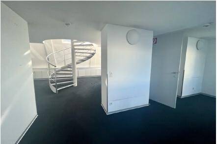 Heller Büroraum mit dunklem Teppichboden und einer auffälligen weißen Wendeltreppe.