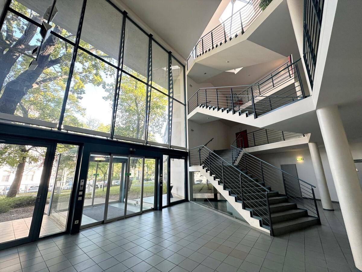 Heller und geräumiger Eingangsbereich mit hoher Decke, großen Glasfronten und einer modernen Treppenanlage.