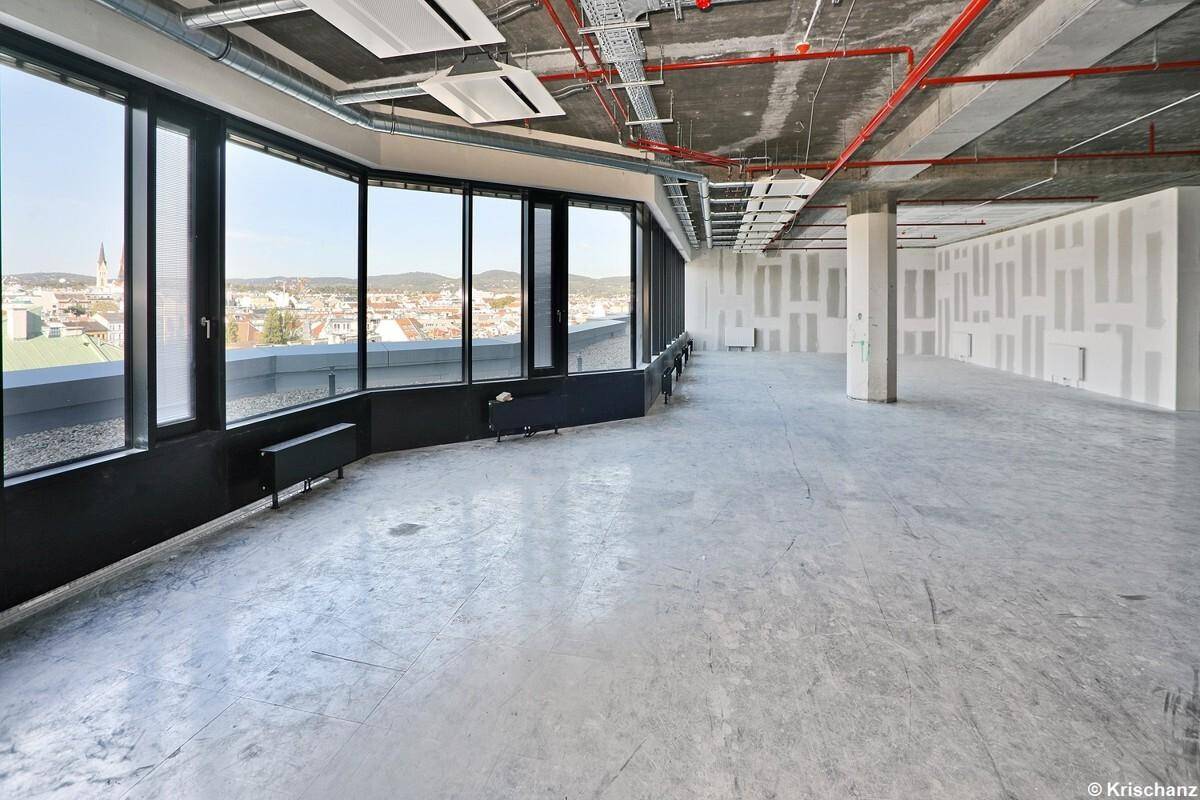 Weitläufiger Bürobereich mit unverputzten Wänden und Decken, großen Fenstern und einem weiten Blick über die Stadt.