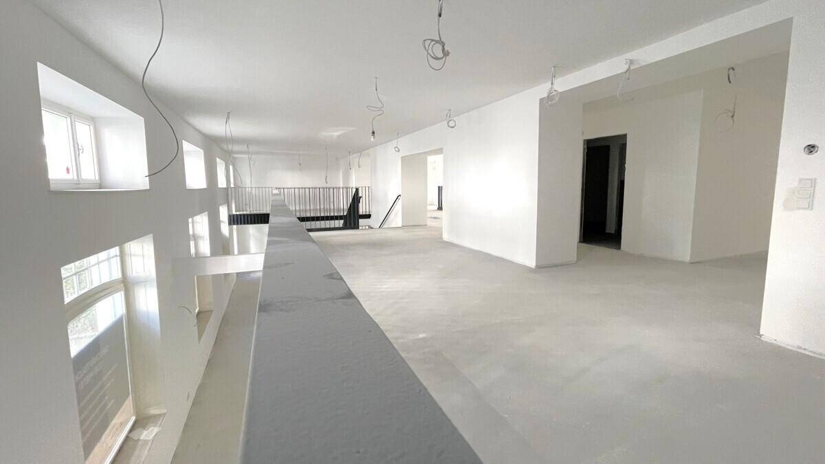 Weitläufiger, heller Raum mit hohen Decken, großen Fenstern und einer Galerieebene.