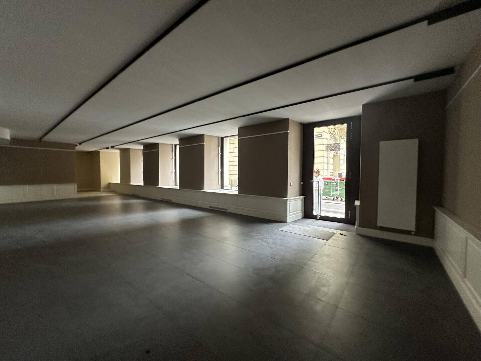 Weitläufiger Geschäftsraum mit hohen Decken und Blick auf die belebte Straße durch große Fenster.