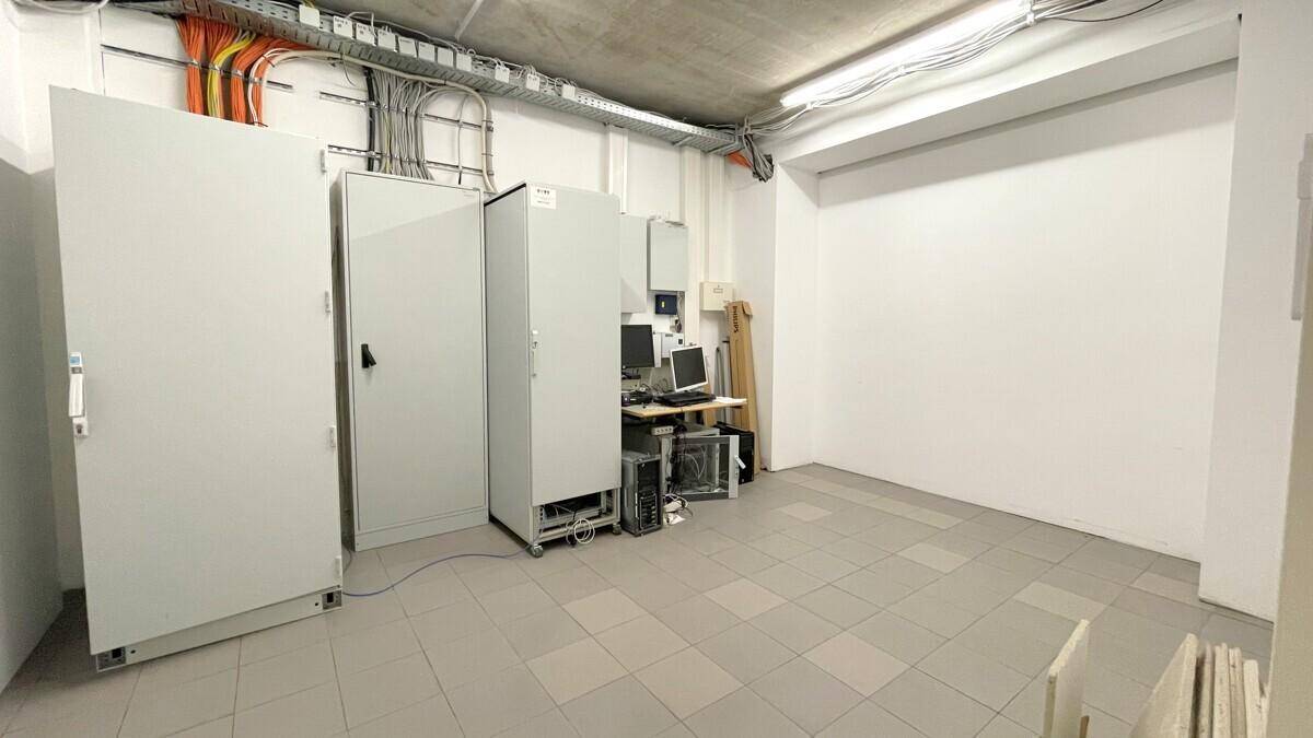 Technikraum mit Serverschränken, Computern und sichtbarer Verkabelung an der Decke.
