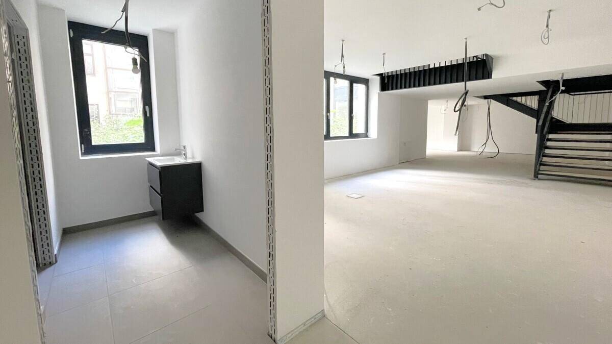 Offener Gewerberaum mit separatem Badbereich, Waschbecken und großen Fenstern.