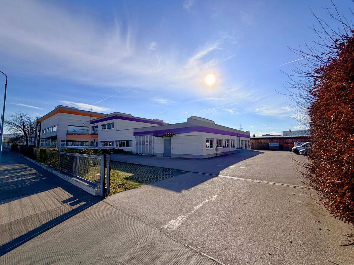 Weitläufige Außenansicht des Geschäftsgebäudes mit großem Parkplatz und umgebender Landschaft unter blauem Himmel.