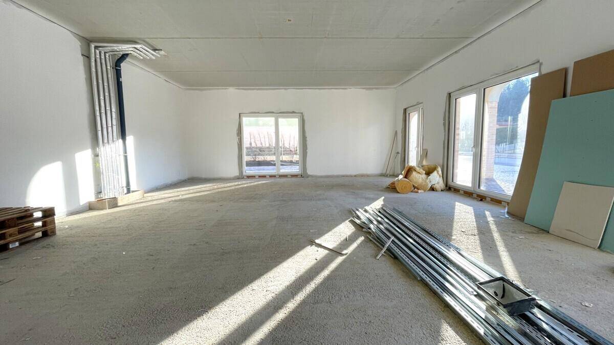 Geräumiger Rohbau mit viel Tageslicht durch mehrere Fenster und Blick auf die Baustelle.