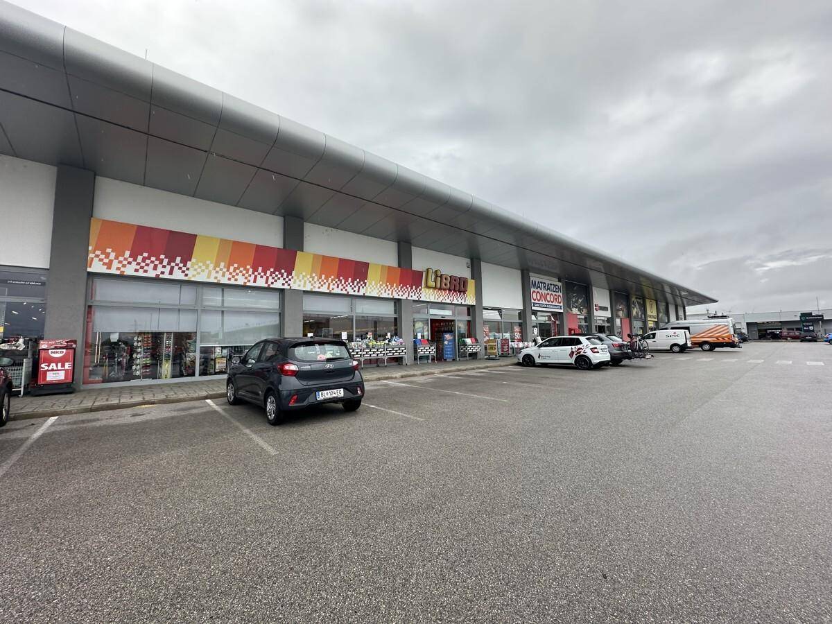 Außenansicht eines modernen Geschäftsgebäudes mit großem Parkplatz unter bewölktem Himmel.