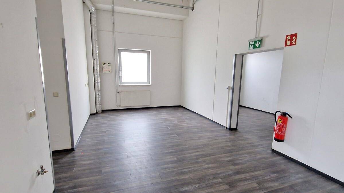 Kleinerer Raum mit Fenster, Heizkörper und Brandschutzvorrichtungen, ideal als Büro oder Lager.