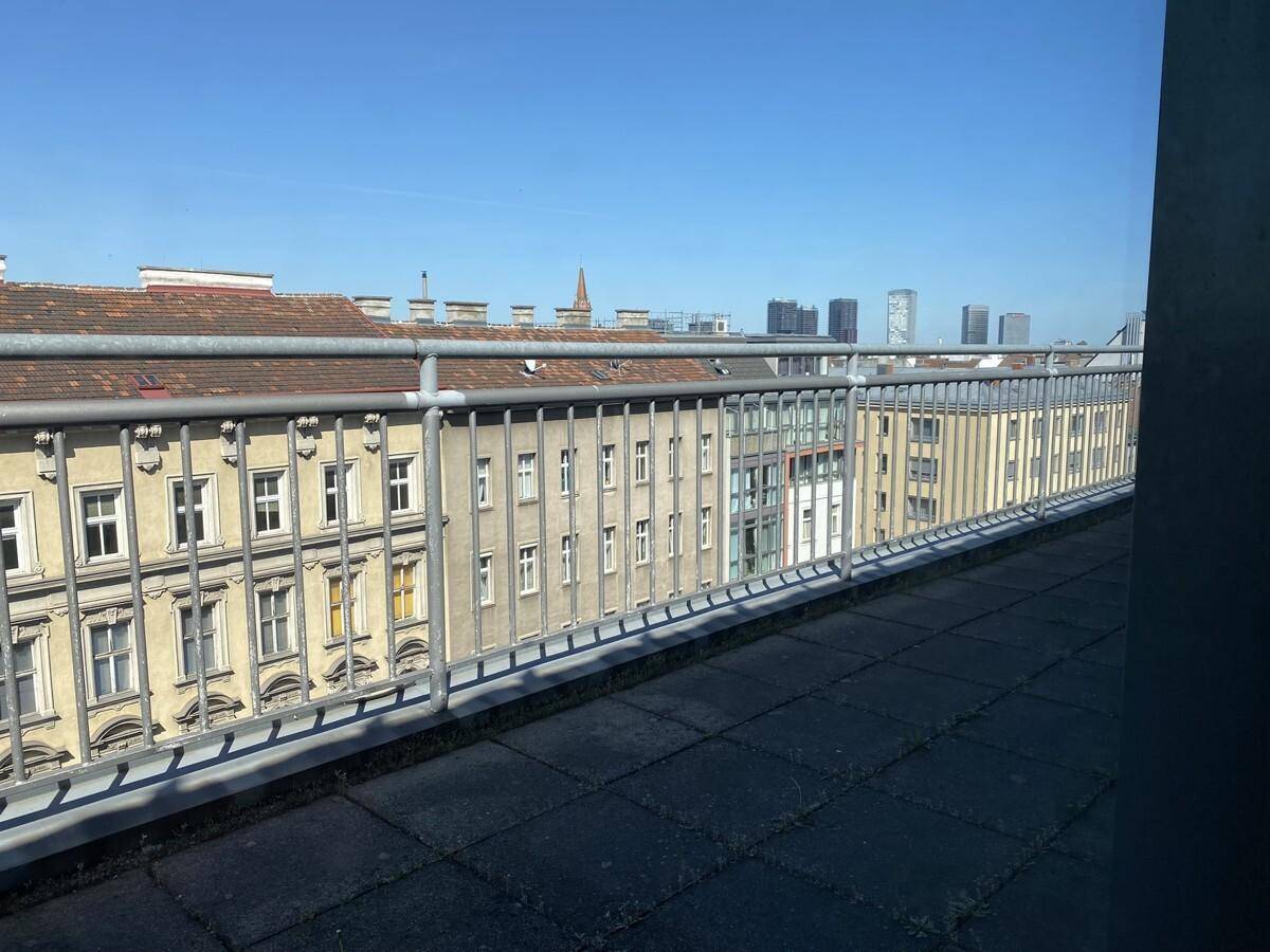 Dachterrasse mit Fliesenboden und Metallgeländer, bietet einen weiten Blick über die Dächer der Stadt.