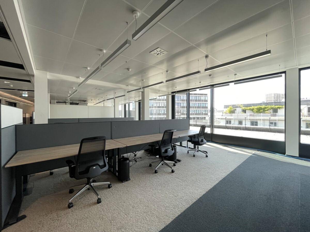 Heller, moderner Büroraum mit Schreibtischen, Bürostühlen und großen Fenstern mit Stadtblick.