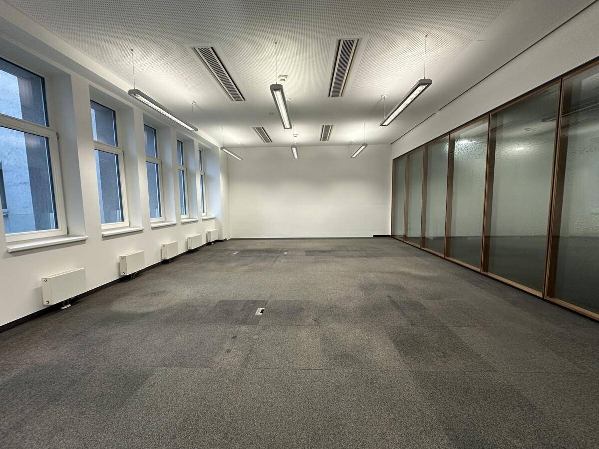 Geräumiger Bürobereich mit Teppichboden, vielen Fenstern und modernen Deckenleuchten, ideal für Großraumbüros.