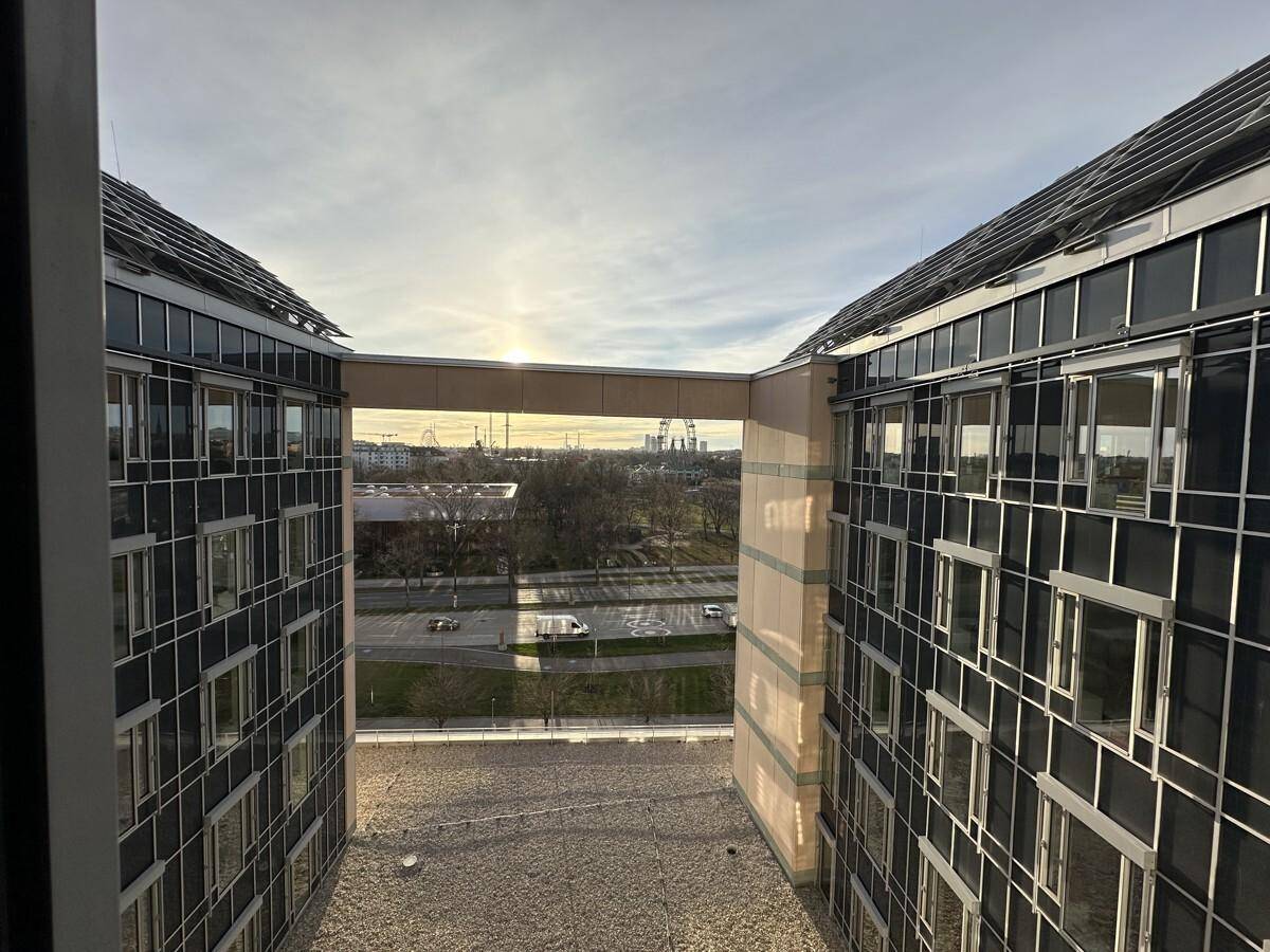 Blick zwischen zwei modernen Gebäudeflügeln mit einer Verbindungsbrücke und Fernsicht in die Umgebung.
