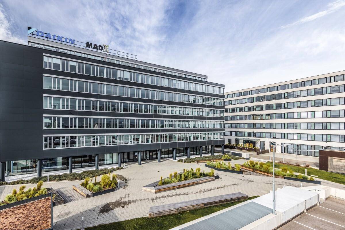 Ansicht des modernen Bürokomplexes mit weitläufigen Fensterfronten und begrünten Außenbereichen.