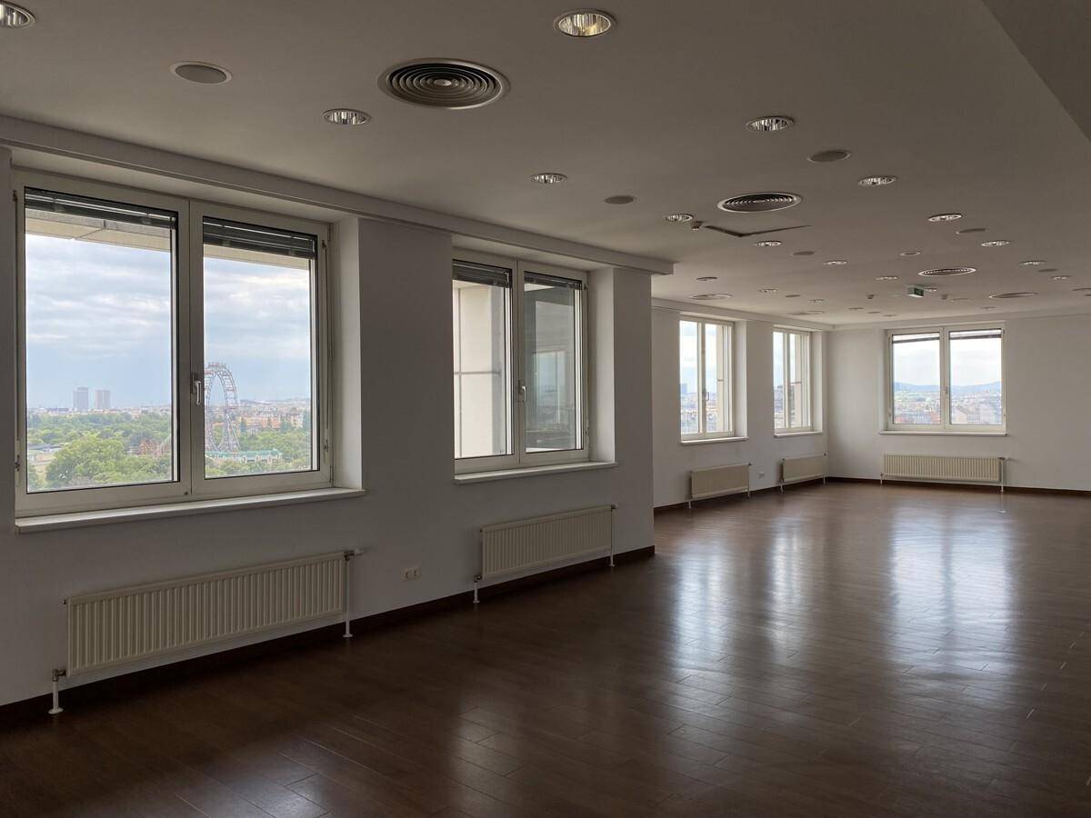 Großer Büroraum mit glänzendem Holzfußboden, vielen Fenstern und Einbaustrahlern.