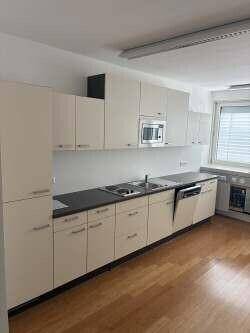 Eine moderne Einbauküche mit hellen Schränken, Spüle, Mikrowelle und Geschirrspüler in einem Bürobereich.