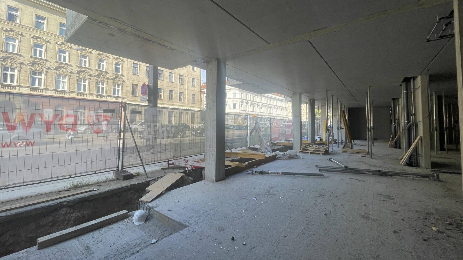 Innenansicht einer Baustelle mit Betonboden, Säulen und Blick auf die Straße durch die offene Fassade.