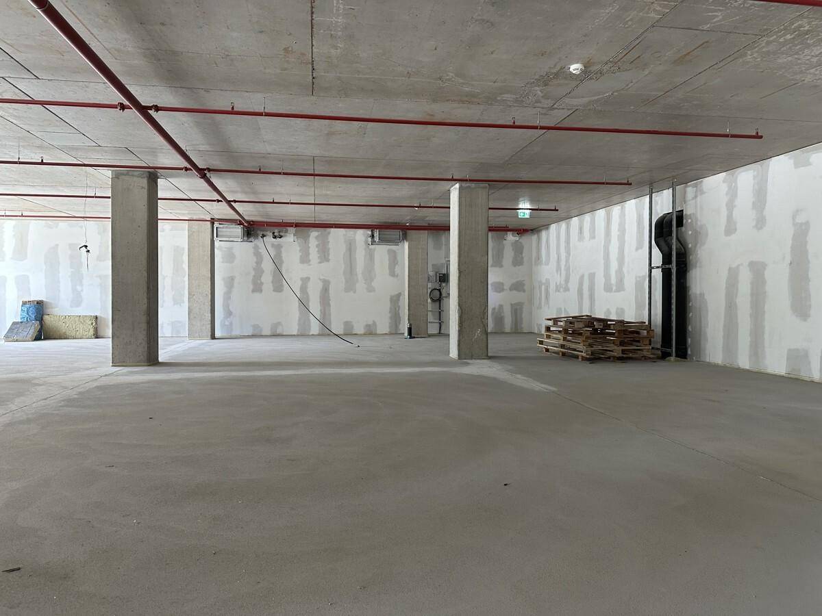 Ein großer, leerer Raum mit Betonboden, Säulen und sichtbaren roten Rohren an der Decke.