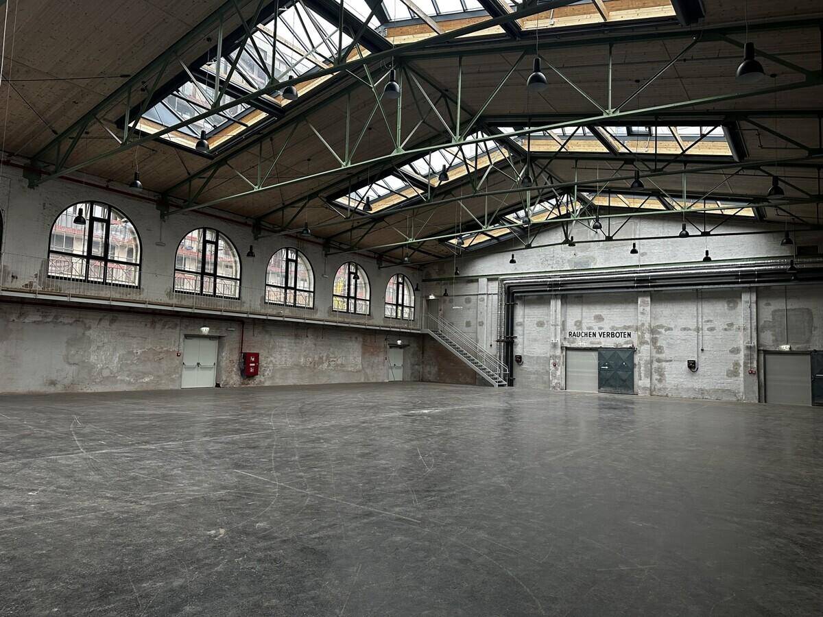 Geräumige Industriehalle mit hohen Decken, Oberlichtern und sichtbaren Stahlträgern.