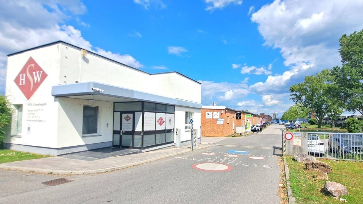 Weißes Geschäftsgebäude mit Eingangsbereich und Zufahrt unter blauem Himmel in einem Gewerbegebiet.