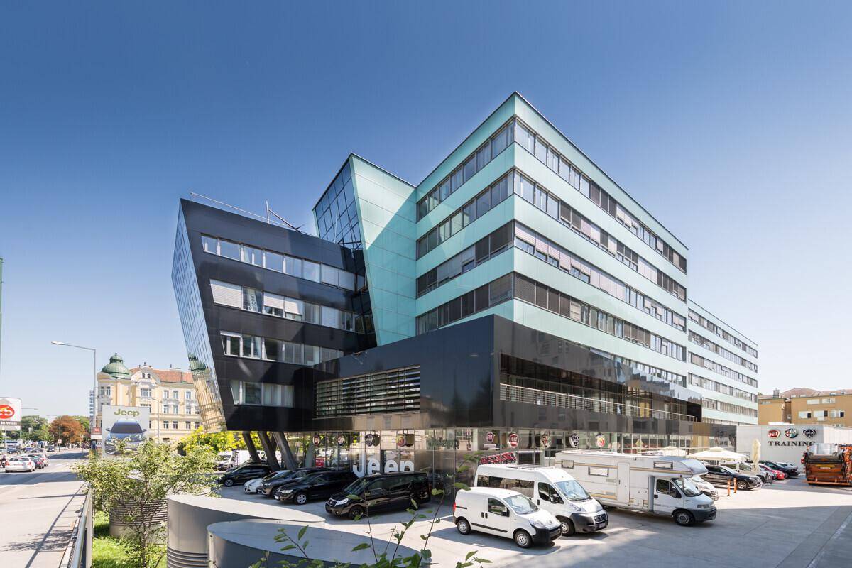 Seitenansicht des modernen Bürogebäudes mit markanten hellblauen und schwarzen Fassadenelementen sowie Parkmöglichkeiten.