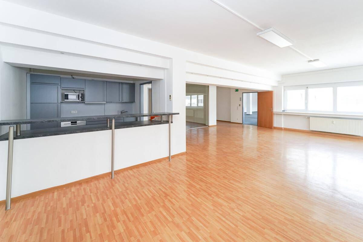 Geräumiger, leerer Büroraum mit hellem Holzfußboden und einer integrierten Küchenzeile mit Bar.