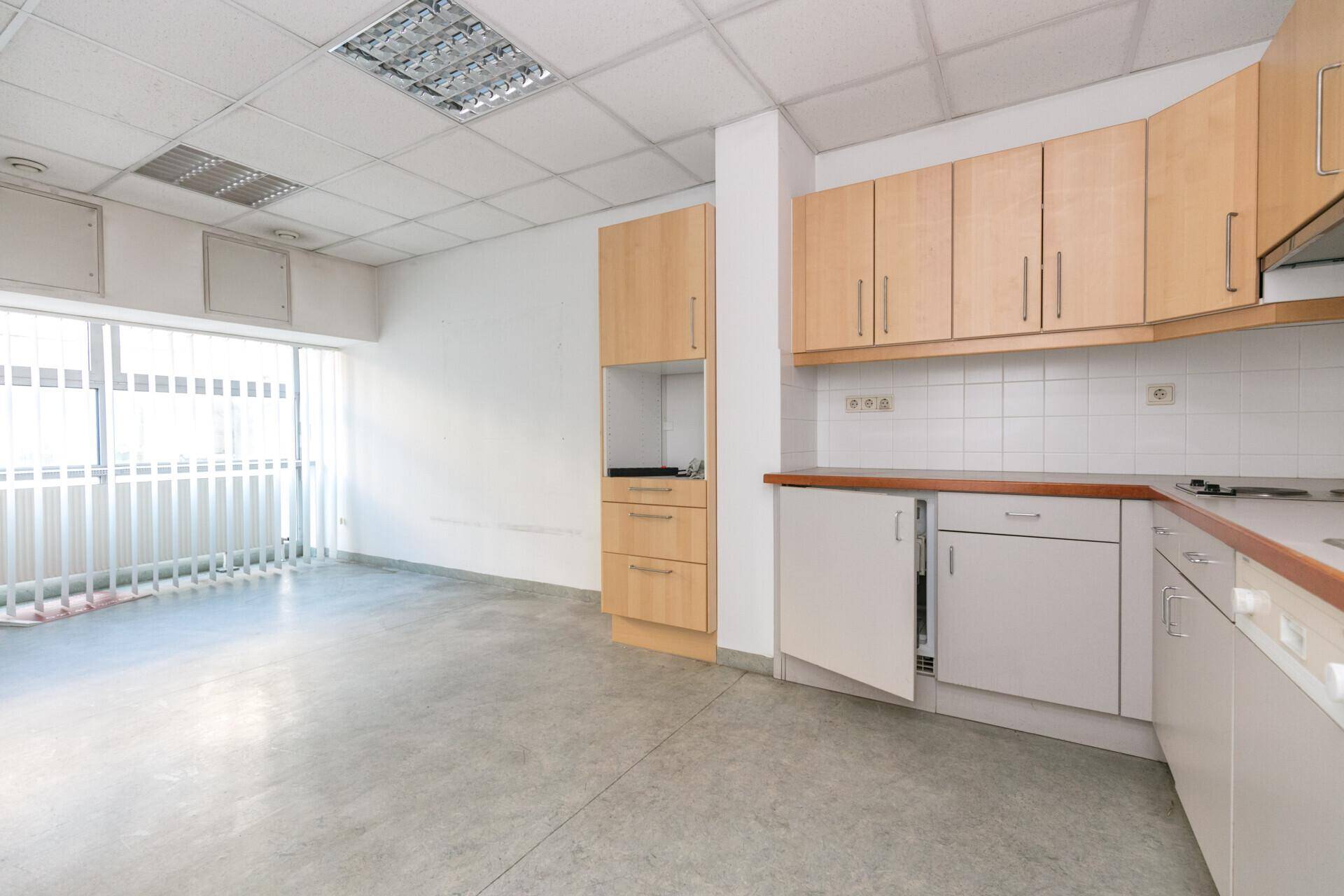 Funktionale Küchenzeile mit hellen Holzschränken, Fliesenrückwand und Fenster mit Jalousien.