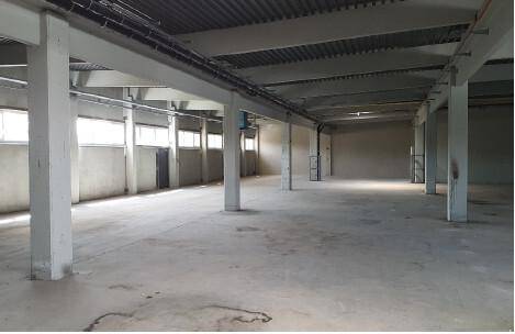 Großer, leerer Industrieraum mit Betonboden, vielen Stützpfeilern und Fenstern für natürliches Licht.
